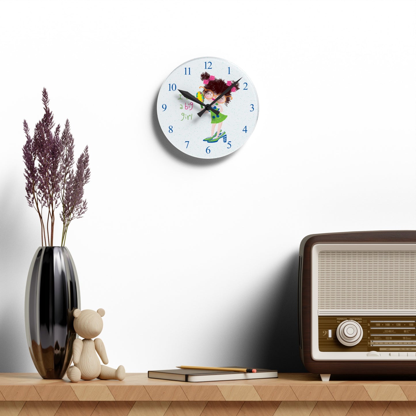 Humorous nursery acrylic wall clock hanging on a white wall featuring a cartoon girl with curly hair, oversized glasses, and a green dress, holding a mirror, with the text 'I am a big girl' alongside blue numbers on the clock face - on the wall, size 8”x8” (square ), kidlic