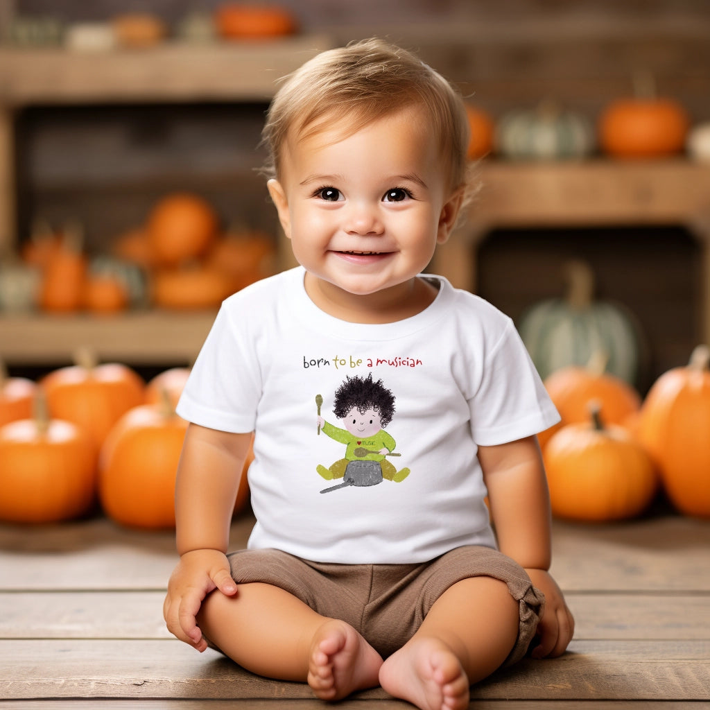 Cute preschool boy sitting on the floor wearing tee featuring a cartoon baby boy playing a pot with a wooden spoon, with the text 'Born to be a musician’, free shipping, USA, kidlic