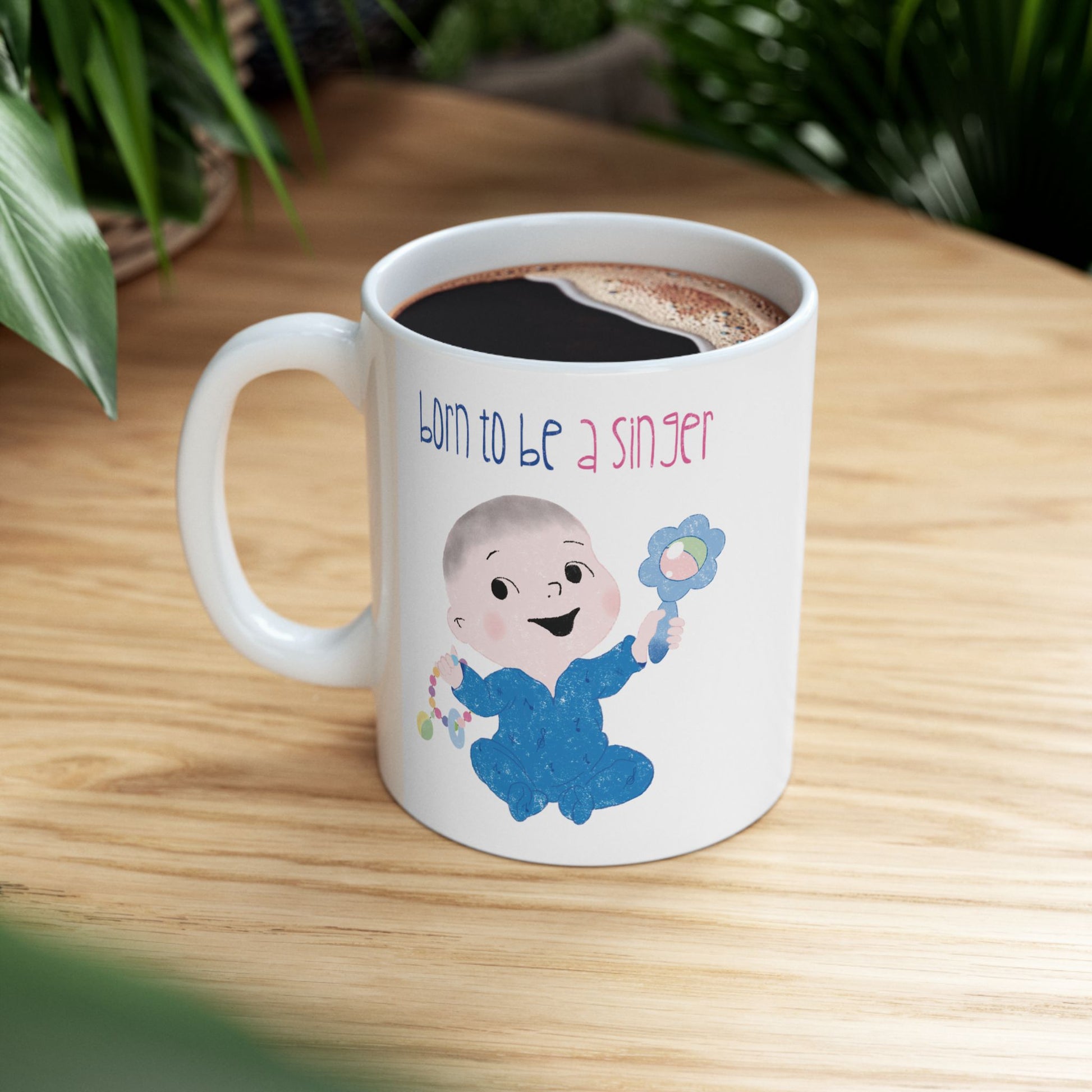 Playful nursery coffee mug featuring a cartoon baby boy holding a rattle, with the text "Born to be a singer”, on a small table, size: 11oz, Kidlic