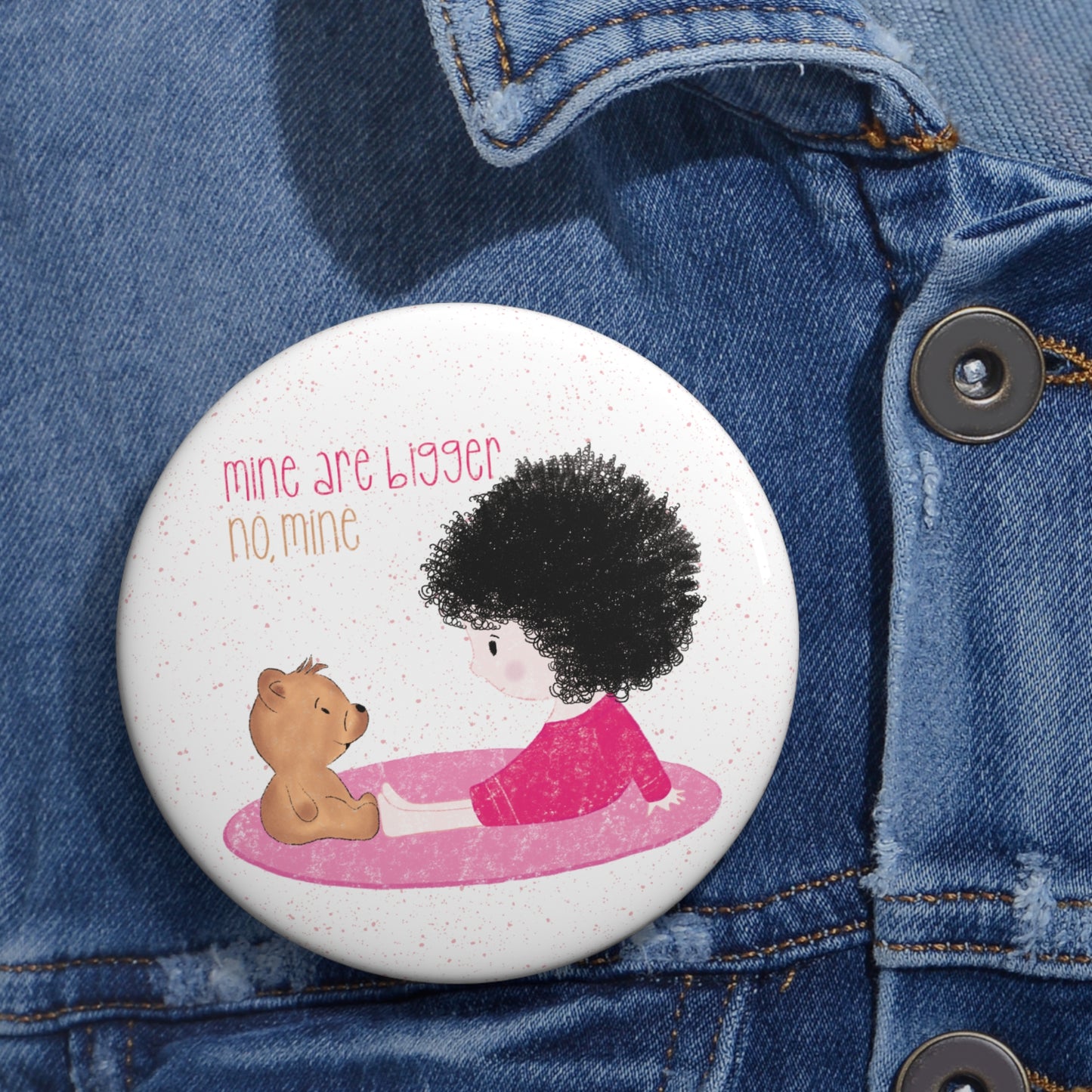 Playful nursery pin button featuring a cartoon child and a stuffed bear sitting on a pink mat, with the text 'mine are bigger,  no, mine’, size 3”, close-up, kidlic