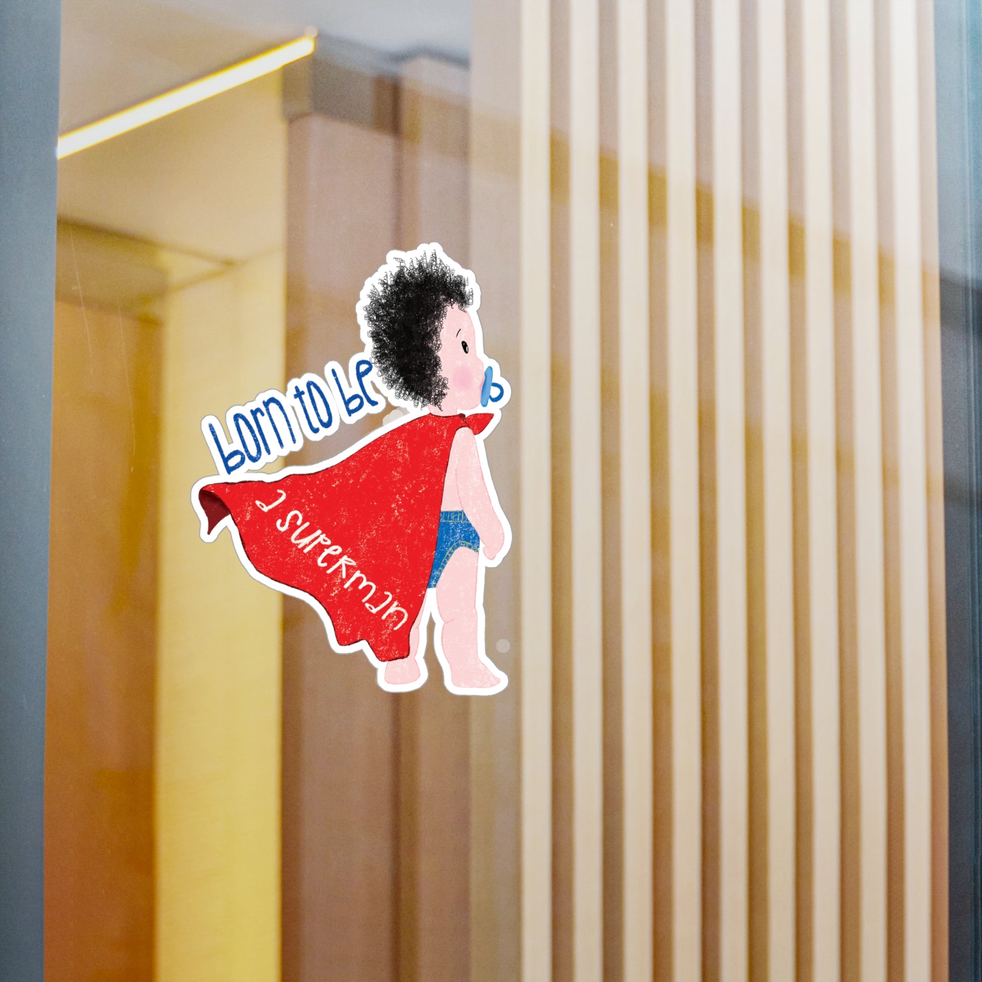 Amusing nursery vinyl wall decal featuring a cartoon baby with a pacifier, wearing a red cape, with the text 'Born to be a superman’, size 6”x8”, close-up on the wall, kidlic
