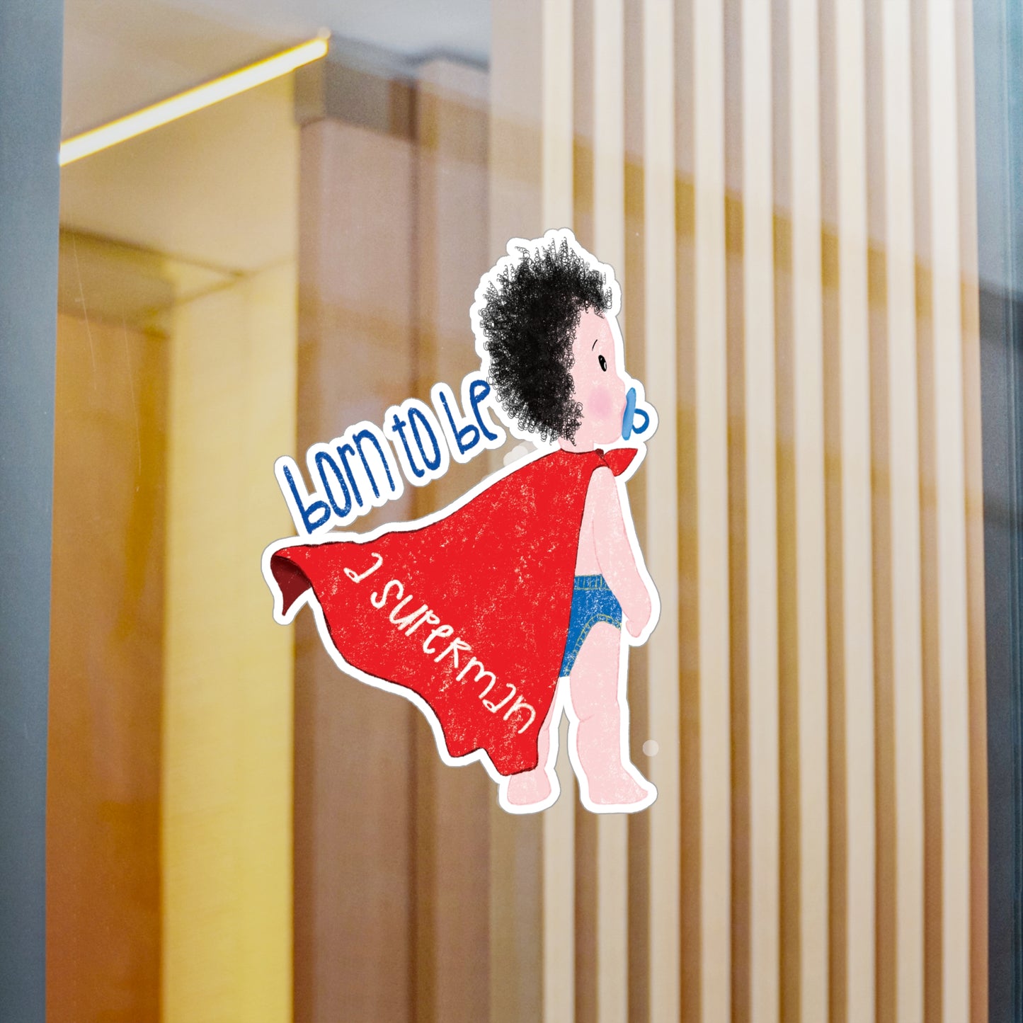 Playful nursery vinyl wall decal featuring a cartoon baby with a pacifier, wearing a red cape, with the text 'Born to be a superman’, size 8”x10”, close-up on the wall, kidlic
