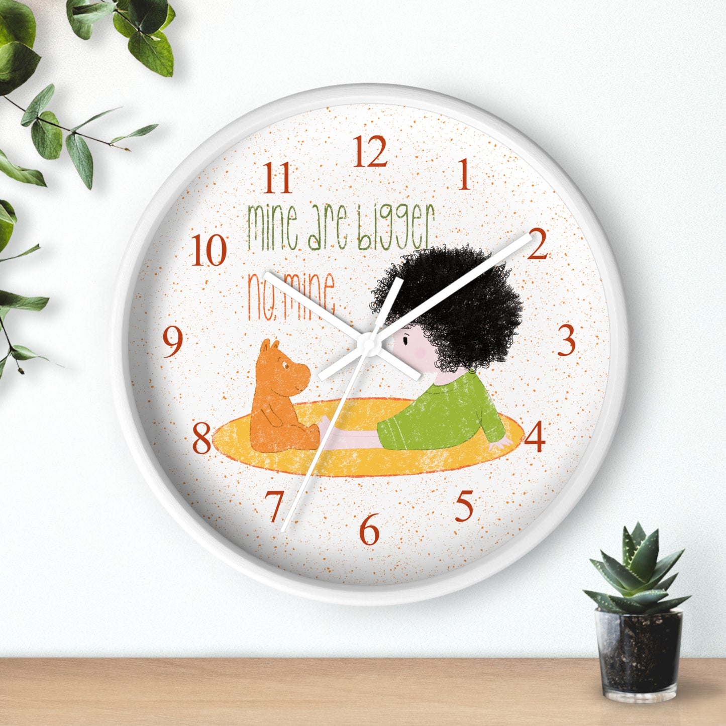 Funny 10” sized white round wall clock with white hands featuring a cartoon child sitting on a yellow mat, facing a stuffed bear, with the text 'mine are bigger' and 'no, mine,' and orange numbers on the clock face, kidlic