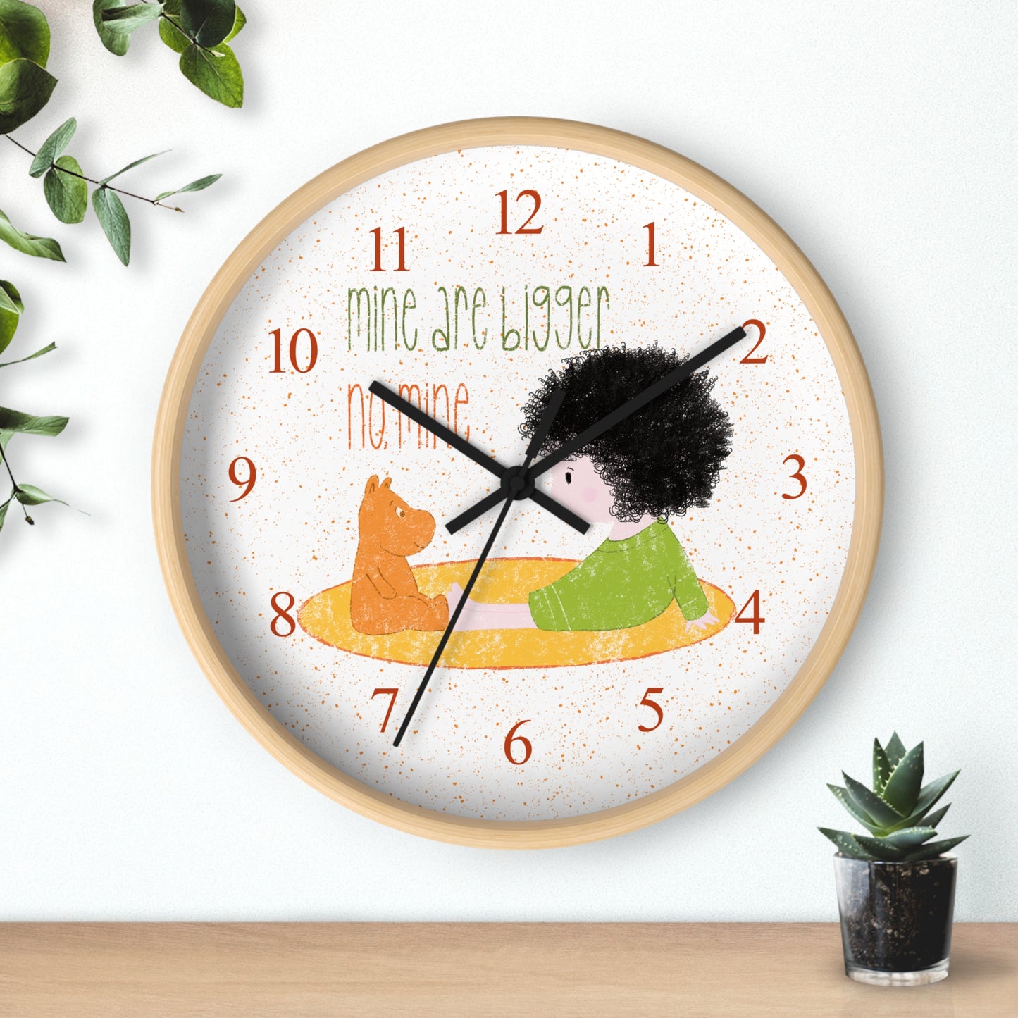 Funny 10” sized wooden round wall clock with black hands featuring a cartoon child sitting on a yellow mat, facing a stuffed bear, with the text 'mine are bigger' and 'no, mine,' and orange numbers on the clock face, kidlic