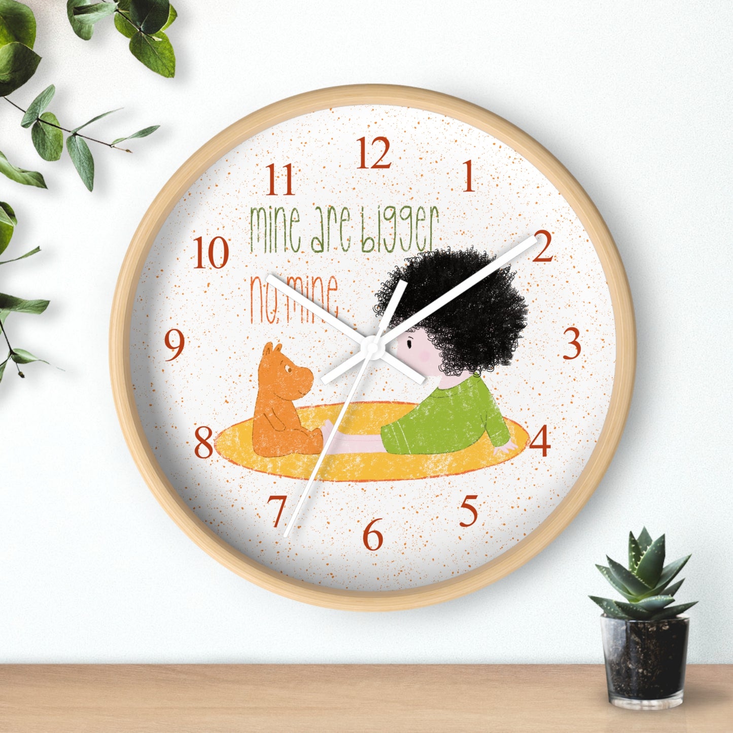 Funny 10” sized wooden round wall clock with white hands featuring a cartoon child sitting on a yellow mat, facing a stuffed bear, with the text 'mine are bigger' and 'no, mine,' and orange numbers on the clock face, kidlic